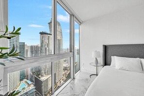 A modern hotel room with a large window, a bed, a nightstand, and a view of a cityscape. - Icon Brickell 2BDR 44th Fl Ocean Views+Spa Access (Miami)