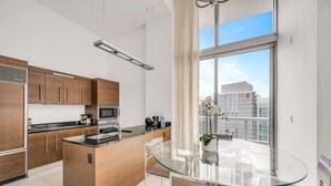 A modern kitchen with a central island, stainless steel appliances, and a glass dining table with a view of the city. - Icon Brickell 2BDR 40th Fl Ocean Views+Spa Access (Miami)