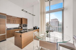 A modern kitchen with a central island, stainless steel appliances, and a glass dining table with a view of the city. - Icon Brickell 2BDR 40th Fl Ocean Views+Spa Access (Miami)