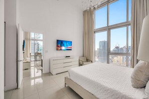 A modern hotel room with a large bed, a flat-screen TV, a dresser, and a view of the cityscape. - Icon Brickell 2BDR 40th Fl Ocean Views+Spa Access (Miami)