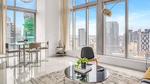 A modern living room with a glass table, a chair, a potted plant, and a view of the cityscape through large windows. - Icon Brickell 2BDR 40th Fl Ocean Views+Spa Access (Miami)