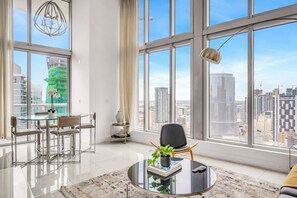 A modern living room with a glass table, a chair, a potted plant, and a view of the cityscape through large windows. - Icon Brickell 2BDR 40th Fl Ocean Views+Spa Access (Miami)