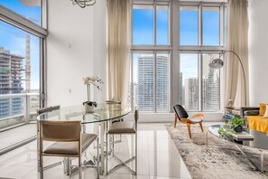 A modern living room with a glass dining table, two chairs, a sofa, a floor lamp, and a view of tall buildings. - Icon Brickell 2BDR 40th Fl Ocean Views+Spa Access (Miami)