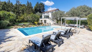 A swimming pool with lounge chairs, a pergola, and a two-story house with a stone facade. - 🌿 Villa Familiale à Quelques Pas du Vieux Mougins (Mougins)