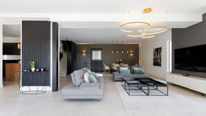 A modern living room with a grey sofa, a coffee table, and a TV. There is a staircase leading to another level. - 🌿 Villa Familiale à Quelques Pas du Vieux Mougins (Mougins)