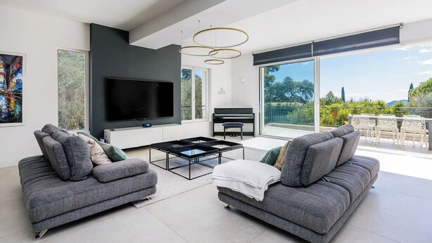 A modern living room with a flat-screen TV, grey sofas, a coffee table, and a piano. - 🌿 Villa Familiale à Quelques Pas du Vieux Mougins (Mougins)