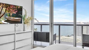 Un dormitorio moderno con un amplio ventanal, un cuadro de un barco y vistas al agua.