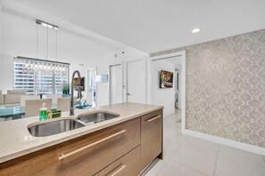 A modern kitchen with a large island, stainless steel sink, and wooden cabinetry. - Icon Brickell - 2BED/1BATH - Bay Views (Miami)