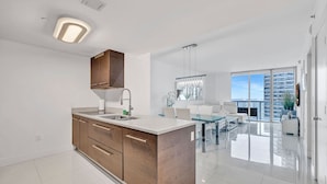 Una cocina moderna con una isla central, un comedor con mesa de vidrio y vistas a la ciudad a través de amplias ventanas.