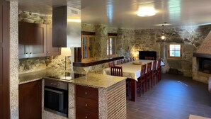 Eine Küche mit Granitarbeitsplatten, Holzschränken, einer Steinwand, einem Kamin und einem Essbereich mit Stühlen und einem Tisch.