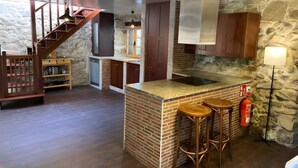 Eine Küche mit einer zentralen Kochinsel, Holzbarhocker, einer Steinwand und einer Treppe.