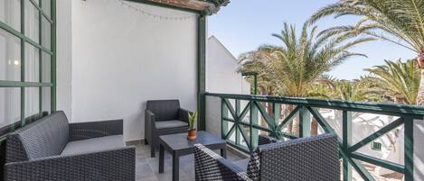 A balcony with wicker furniture, a small table with a plant, and a view of palm trees.