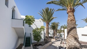 A narrow pathway flanked by white buildings, palm trees, and a small staircase. - Heiwa Apartment with Shared Pool, Shared Garden, and Wi-Fi in Costa Calma (Costa Calma)