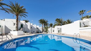 A swimming pool with clear blue water, surrounded by white buildings and palm trees. - Heiwa Apartment with Shared Pool, Shared Garden, and Wi-Fi in Costa Calma (Costa Calma)