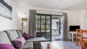 A modern living room with a sofa, a wooden coffee table, a TV, and a balcony with a view. - Heiwa Apartment with Shared Pool, Shared Garden, and Wi-Fi in Costa Calma (Costa Calma)