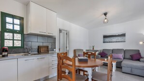 A modern kitchen with white cabinets, a dining table with chairs, a grey sofa, and a painting on the wall. - Heiwa Apartment with Shared Pool, Shared Garden, and Wi-Fi in Costa Calma (Costa Calma)