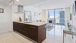 Een moderne keuken met een groot eiland, een eetgedeelte met een glazen tafel en uitzicht op hoge gebouwen.