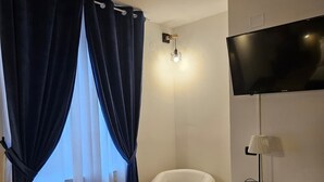 Hotelkamer met een bed, een bureau met lamp, een televisie, een stoel en een raam met gordijnen.