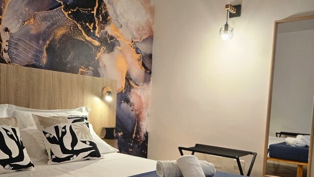 Een hotelkamer met een groot abstract schilderij aan de muur, een netjes opgemaakt bed met handdoeken, een ronde tafel en een spiegel.