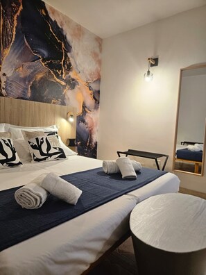Habitación de hotel con un cuadro abstracto grande en la pared, una cama bien hecha con toallas, una mesa redonda y un espejo.