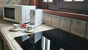 Een keuken met een magnetron, broodrooster en elektrische kookplaat, met een betegelde spatwand en een raam.