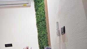 Een kamer met een houten bankje, een klein tafeltje met decoratieve spullen, een wandairconditioner en een verticale groene wandtuin.