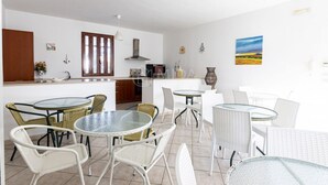 Een moderne keuken met witte kasten, een houten deur en een eethoek met witte rieten stoelen en glazen tafels.