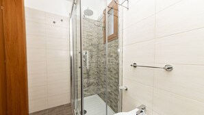 Een badkamer met een glazen douchecabine, een wit wastafeltje en een houten deur.