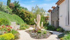 Ein Garten mit einem großen Kaktus, einem Kiesweg und einem weißen Gebäude mit einem Holzbalkon.