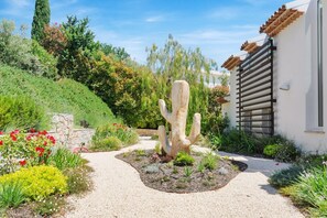 Ein Garten mit einem großen Kaktus, einem Kiesweg und einem weißen Gebäude mit einem Holzbalkon.