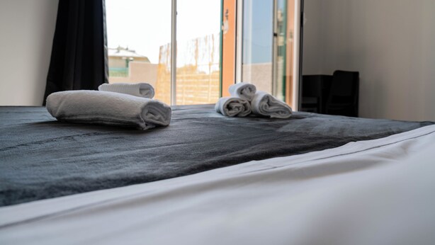 A hotel room with a bed, two rolled towels, a window, and a view of buildings outside. - Oasis of Peace in the Middle of Town: Modern, Quiet and Close to Transportation (Genova)