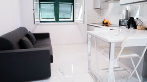 A modern kitchen with a dining area, a sofa, and a window with blinds. - Oasis of Peace in the Middle of Town: Modern, Quiet and Close to Transportation (Genova)