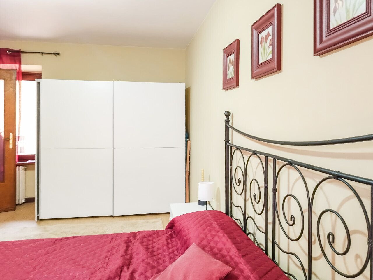 A bedroom with a bed, a wardrobe, a nightstand, and a lamp.