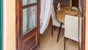 Una mesa de madera con sillas, una ventana con cortinas y una cocina al fondo.