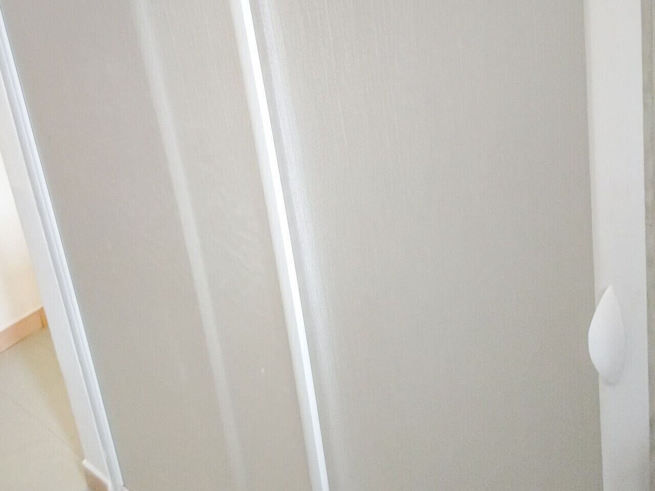 A white door with a handle, a white wall, and a wooden floor.