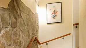 Una escalera con pared de piedra, barandilla de madera y un cuadro abstracto enmarcado.