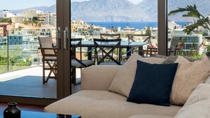 Un balcon aménagé avec un canapé, des fauteuils et une table, offrant une vue sur un paysage urbain avec des montagnes et la mer.