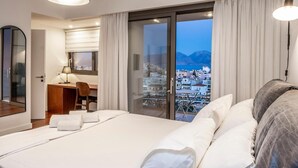 Une chambre d’hôtel avec un lit, un bureau, une chaise, une lampe et une vue sur le paysage urbain, visible à travers une grande fenêtre.