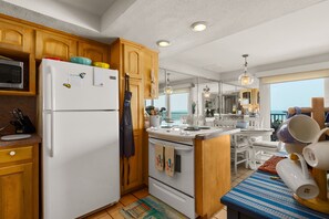 A kitchen with wooden cabinets, a white refrigerator, a microwave, and a dining area with a view. - Beachfront Gem with Pool, Hot tub, Gym (South Padre Island)