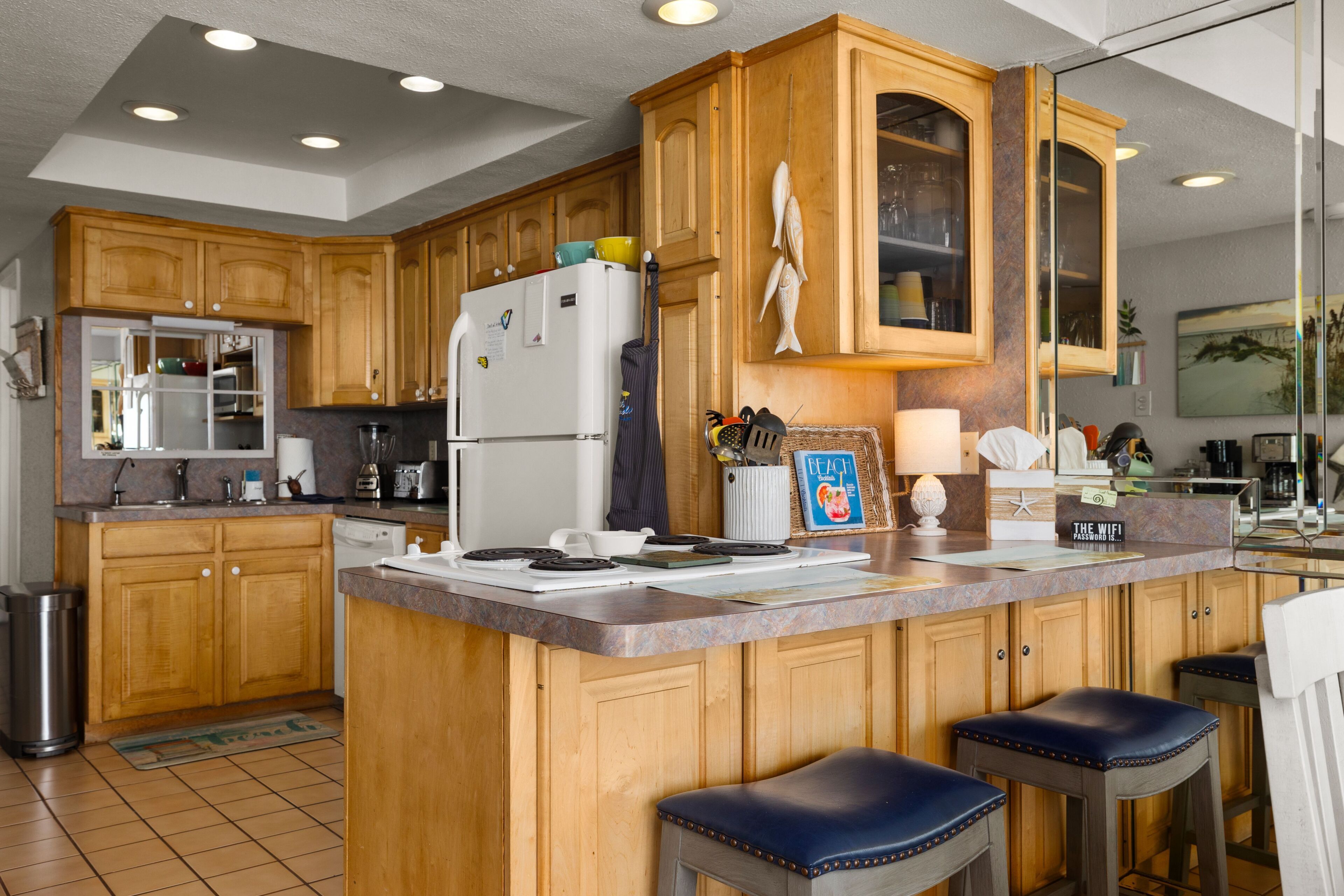 A kitchen with wooden cabinets, a refrigerator, a stove, and bar stools.