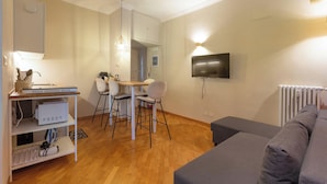 Un salon moderne avec un canapé gris, un coin repas comprenant une table et des chaises, un téléviseur fixé au mur et un radiateur.