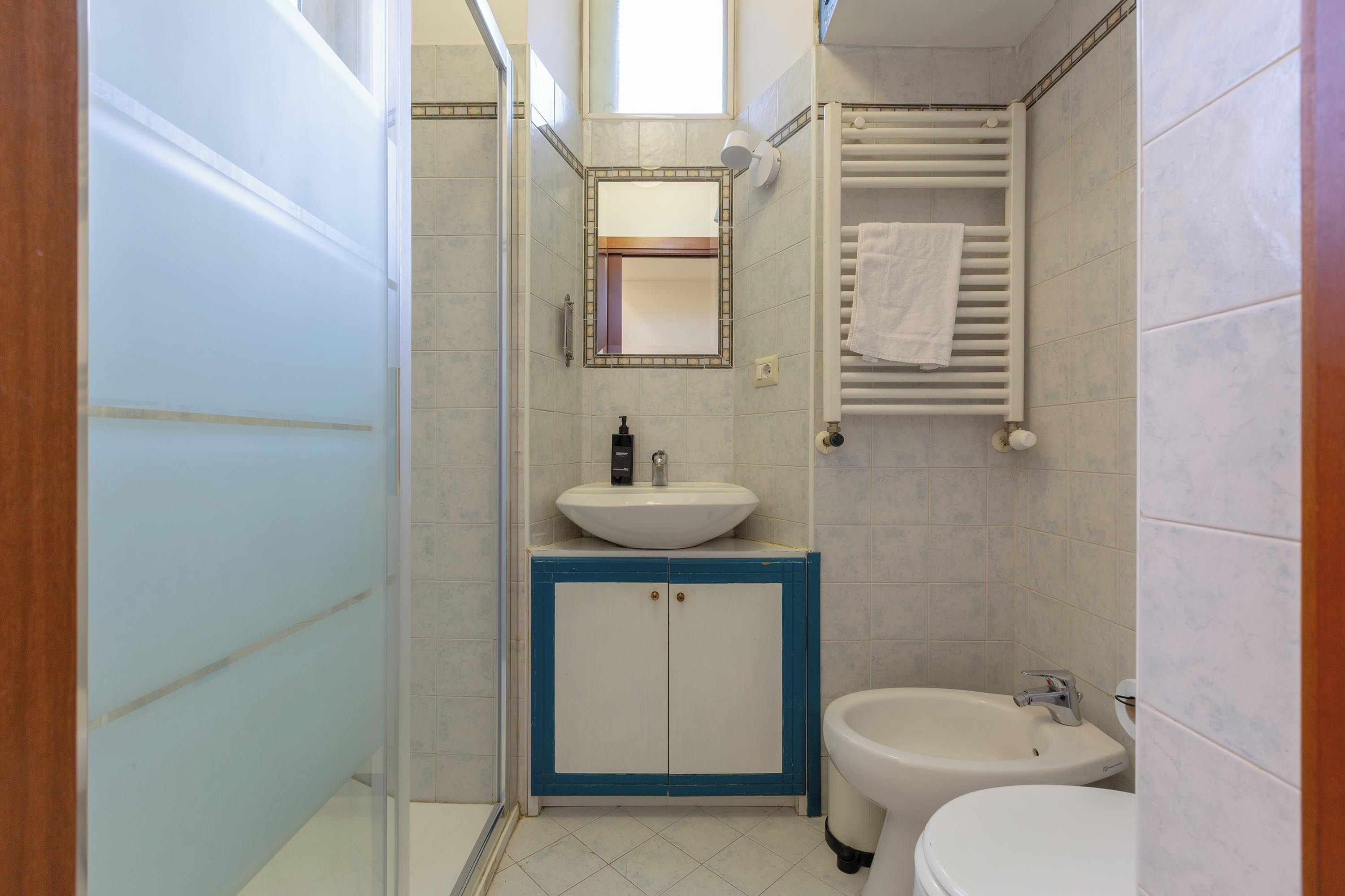 Ein Badezimmer mit einem weißen Waschbecken, einem blauen Schrank, einer weißen Toilette und einem Handtuch an einem weißen Heizkörper.
