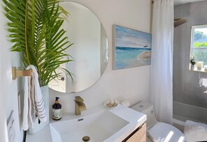 Un bagno con un lavandino bianco, uno specchio, una pianta in vaso, un quadro e un water.