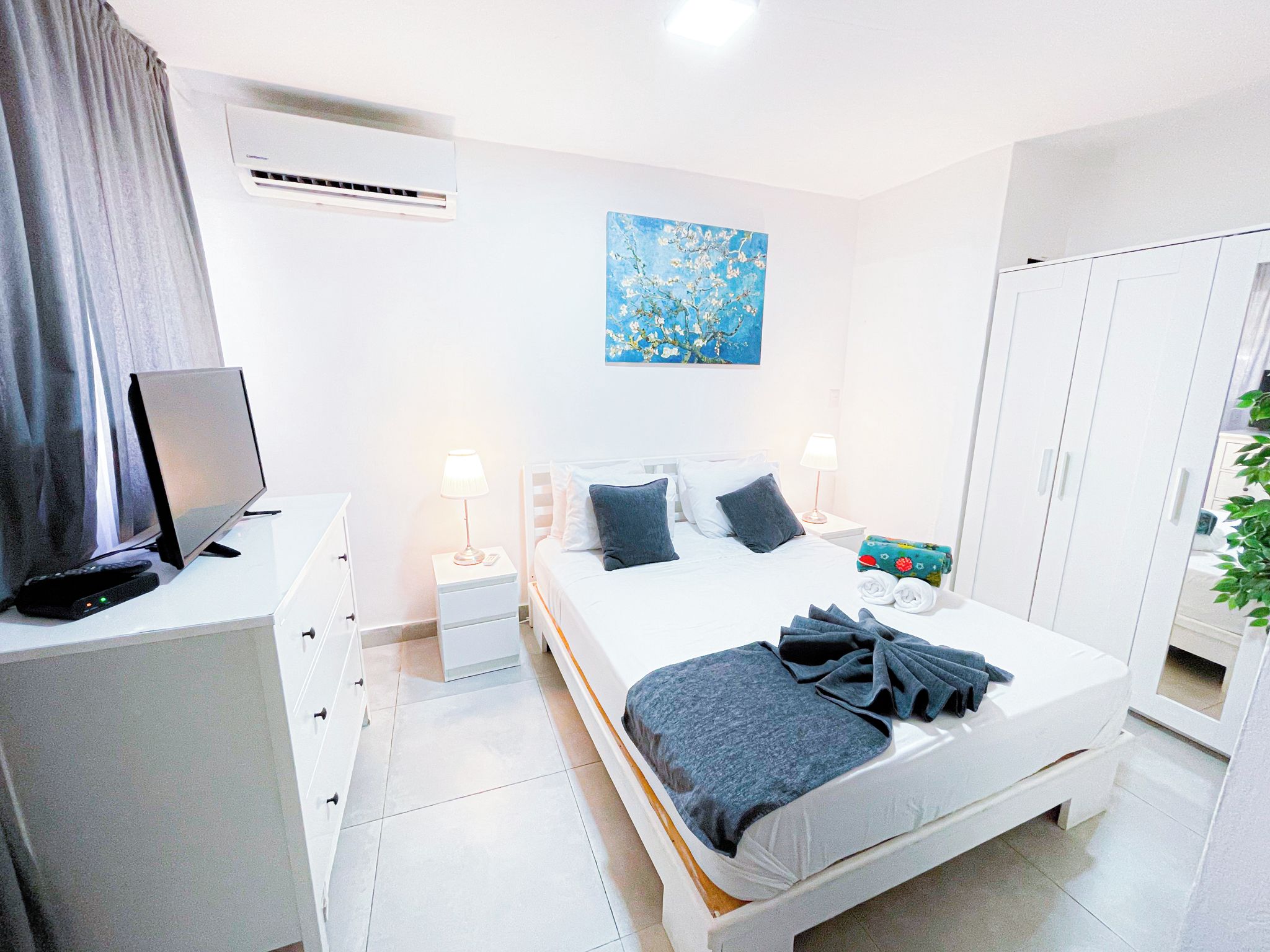 Ett modernt hotellrum med en säng, sängbord, en tv och en tavla på väggen.