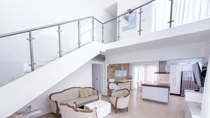 Amplia sala de estar con escalera, sofá, mesa de centro y zona de cocina.