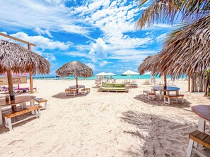 Una spiaggia con ombrelloni di paglia, lettini e un tavolo in legno.