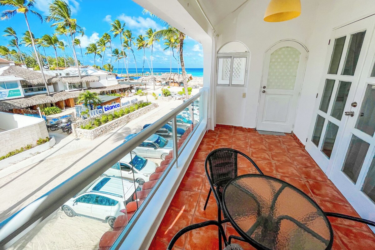 Un balcone con vista sulla spiaggia, auto parcheggiate e un ristorante chiamato 'Blanca Beach Club'.