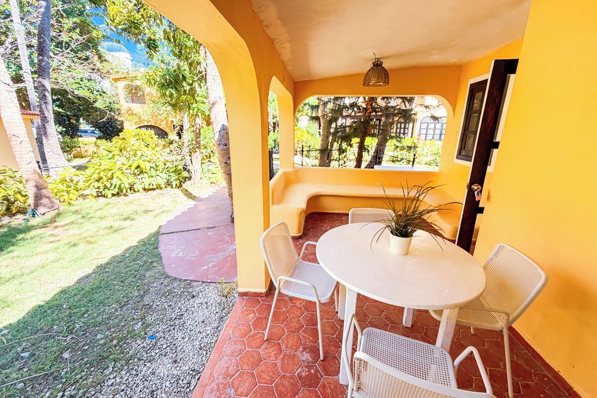 Un portico coperto con un tavolo rotondo e sedie, una panca e una porta.