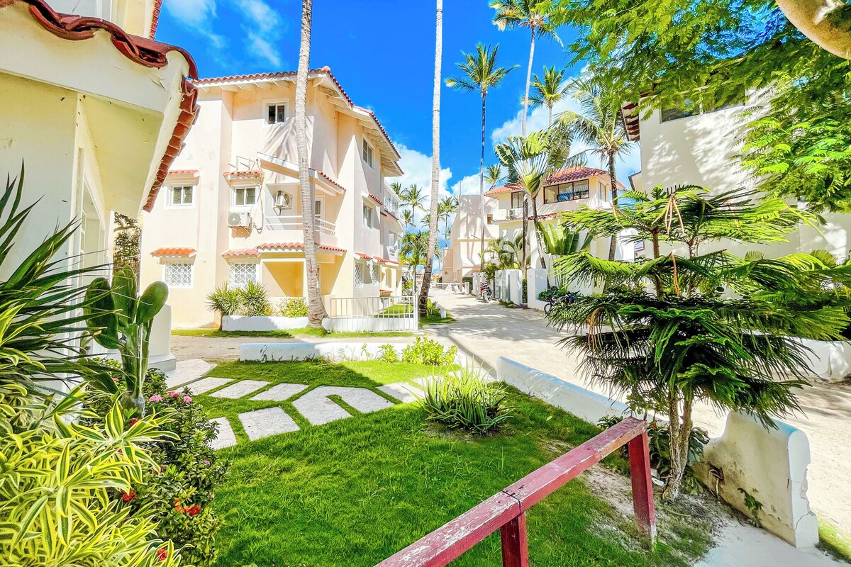 Un quartiere residenziale con un vialetto alberato, palme e un edificio con balconi.