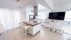 Una cocina moderna con armarios blancos, una isla central y un televisor de pantalla plana montado en la pared.